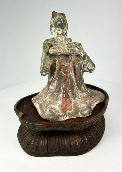 Tang Dynasty terracotta figure of a seated female court musician playing a pan flute, traces of red and white pigments, displayed on a carved wooden stand, 7th–9th century China.
