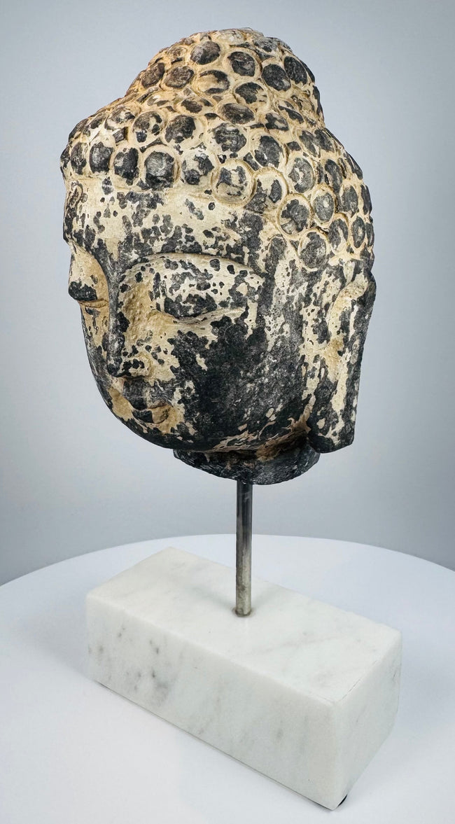 Historic carved stone Buddha head mounted on a modern marble display base