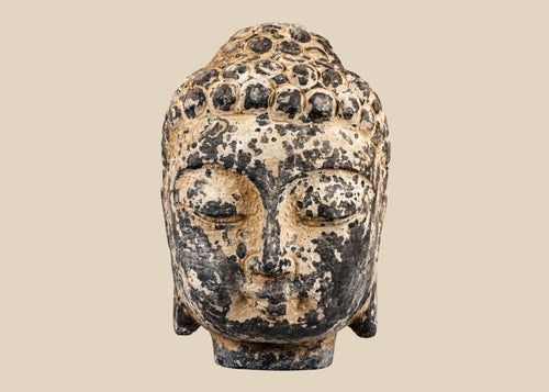 Antique carved stone Buddha head from Southeast Asia, likely Thailand or Cambodia, 18th–19th Century. Features serene meditative expression, curled hair, and traces of original pigments. Mounted on a marble base, reflecting Buddhist artistry, spiritual symbolism, and historical craftsmanship of the region.