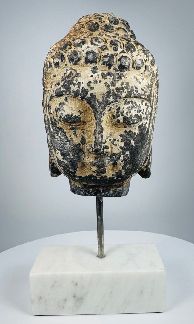 Three-quarter view of antique Buddha head with stylized facial features and curled hair