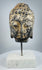 Three-quarter view of antique Buddha head with stylized facial features and curled hair