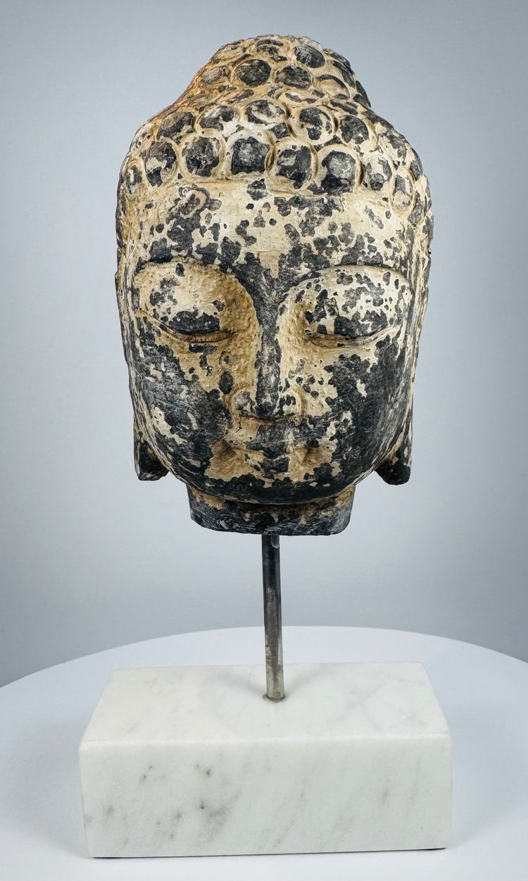 Three-quarter view of antique Buddha head with stylized facial features and curled hair