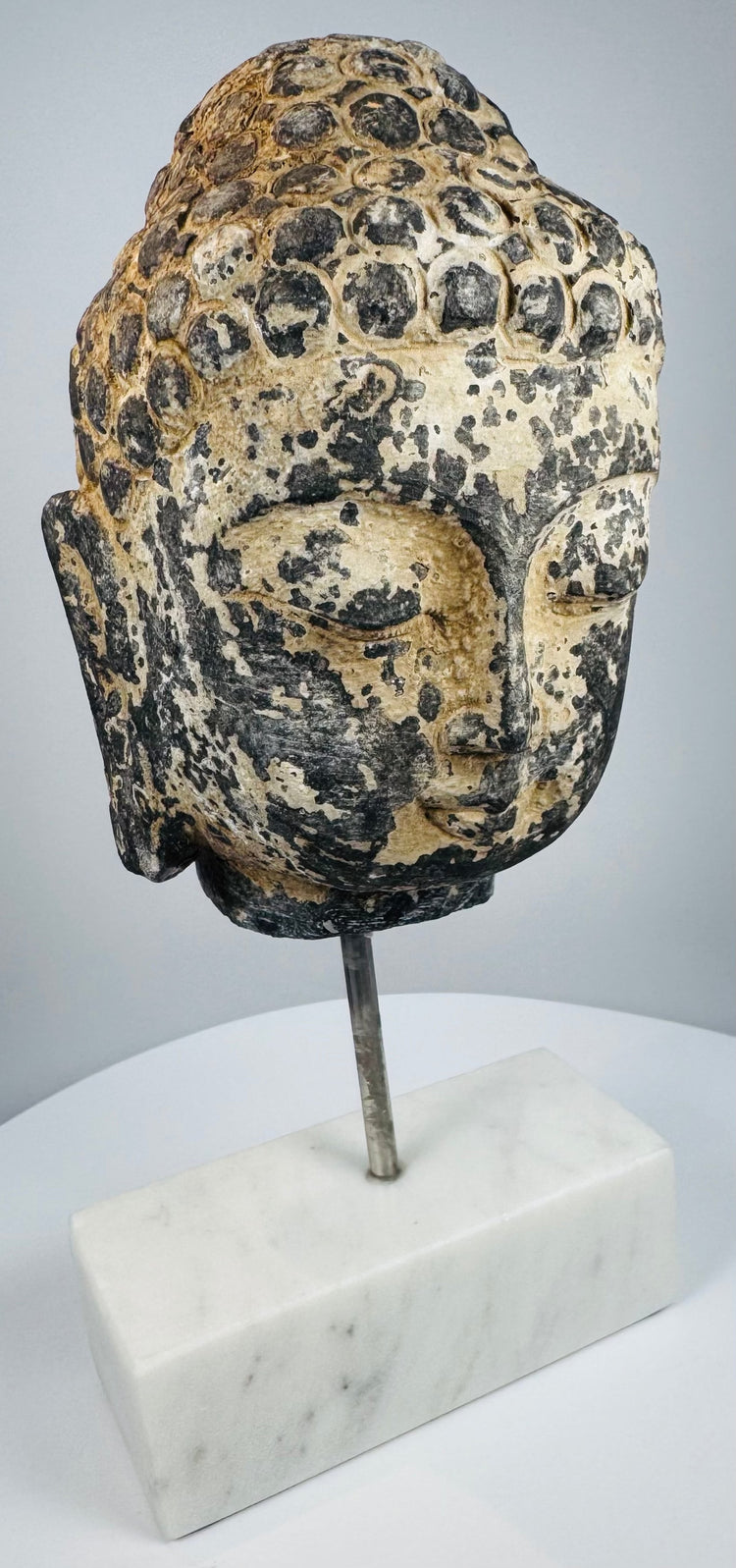 Historic Buddha head sculpture with peaceful expression mounted on a white marble base