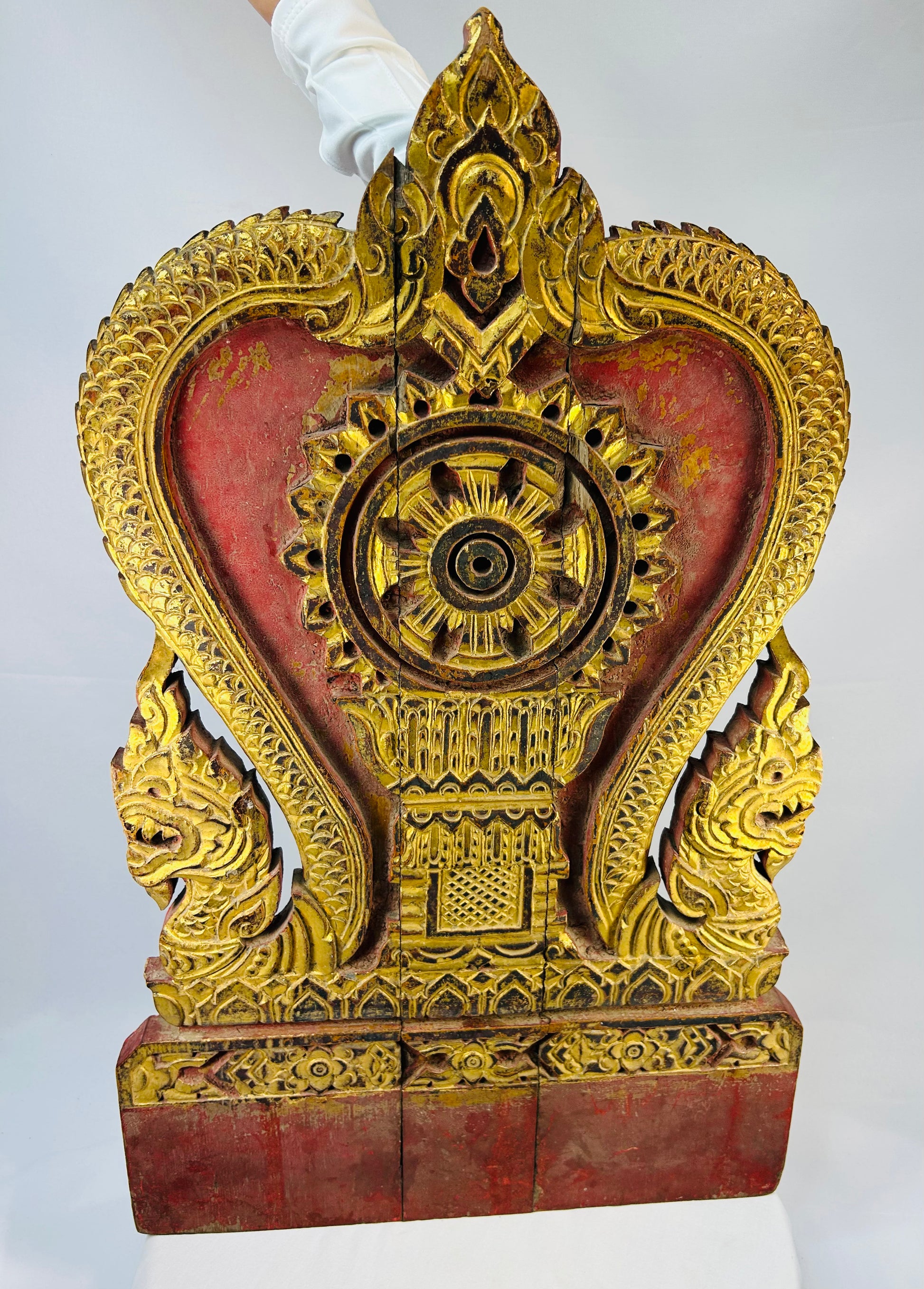 Thai Buddhist shrine panel carved from teakwood, gilded over red lacquer, featuring central dharmachakra and twin naga serpents, late 19th century, Rattanakosin/Lanna tradition, 24.5 x 15 inches