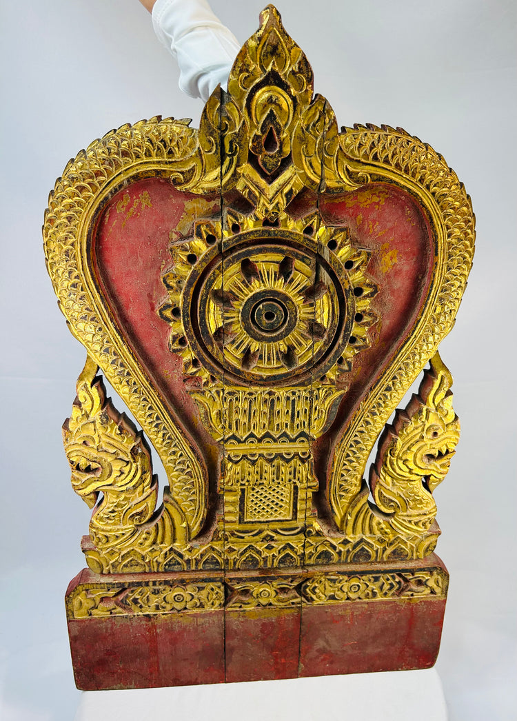 Thai Buddhist shrine panel carved from teakwood, gilded over red lacquer, featuring central dharmachakra and twin naga serpents, late 19th century, Rattanakosin/Lanna tradition, 24.5 x 15 inches