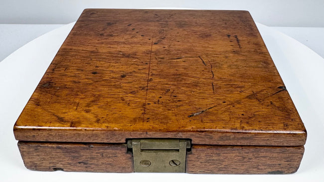 Front edge of the closed antique walnut compass case showing the original dark metal clasp and richly figured wood surface.