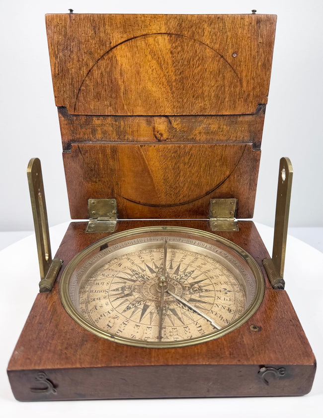 Raised angle of the antique British surveying compass showing the circular instrument seated within its fitted walnut case.