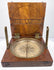 Raised angle of the antique British surveying compass showing the circular instrument seated within its fitted walnut case.