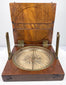 Raised angle of the antique British surveying compass showing the circular instrument seated within its fitted walnut case.