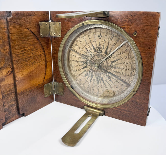Close angled photograph of the 19th-century compass showing its engraved degree ring, needle, brass fittings, and walnut case interior.