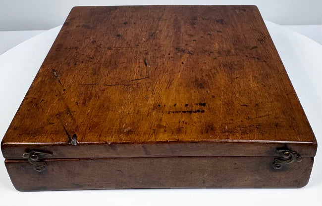 Opposite exterior angle of the walnut instrument case showing its low rectangular profile, hinged construction, and 19th-century surface wear.