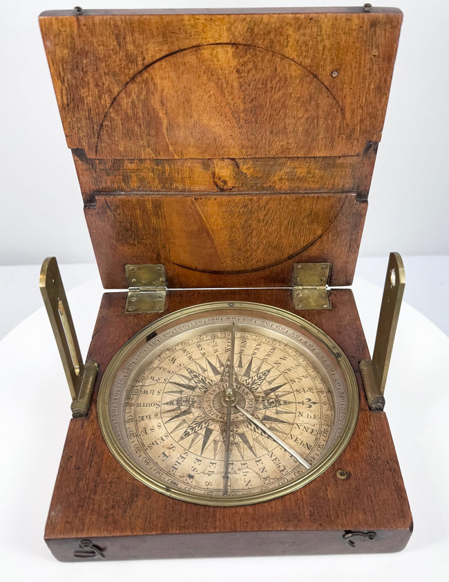 Top-down photograph of the open alidade compass highlighting the silvered degree scale, magnetic needle, and brass sighting components.