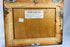 Verso view of painting showing wooden backing, gallery label from Robert McLaughlin Gallery, and deaccession markings.