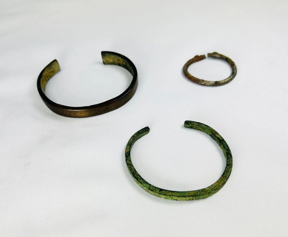 Rare set of three ancient bracelets from the Near East (Mesopotamia to Levant or Anatolia), Bronze to Iron Age (circa 6th millennium BCE – 7th century CE). Includes a broad bronze cuff with green patina, a slender oxidized bronze bracelet, and a textured iron bracelet, reflecting ancient metallurgical skill, decorative traditions, and cultural symbolism of personal adornment.