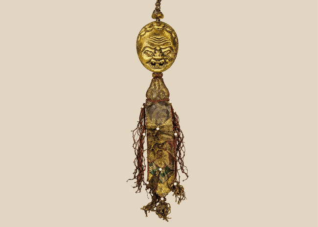 Tibetan Buddhist gilt bronze guardian mask ornament with aged brocade tassels and suspended textile panels