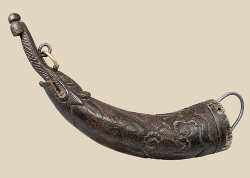 Tibetan bronze ritual powder horn with engraved decorative motifs, curved shape, mounted on a wooden display stand, 19th century.