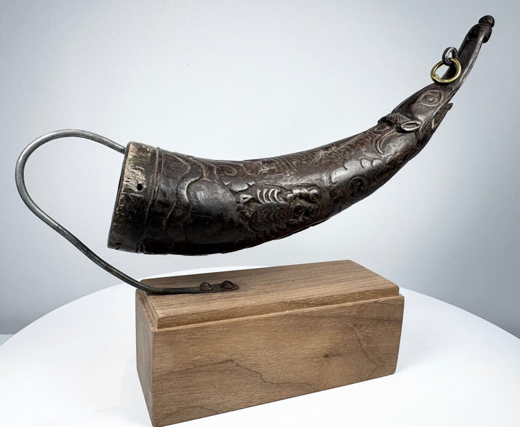Angled view of a Tibetan carved horn ritual implement with decorative body motifs and opening for ritual use.
