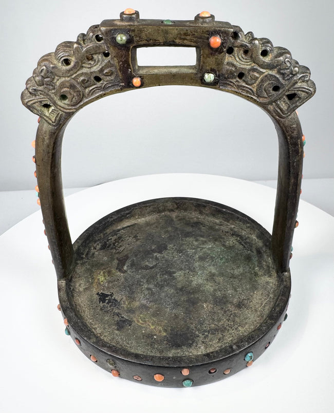 Antique bronze stirrup from the Himalayan region with pierced arch, decorative inlays, and heavy verdigris oxidation.