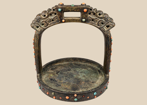 Ornate cast bronze stirrup from Mongolia or Himalayan region, featuring dragon-head terminals, pierced latticework, and hand-set coral, turquoise, and glass inlays, 7 inches tall by 6 inches wide, with natural patina and verdigris, circa 18th century.