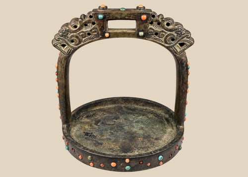 Ornate cast bronze stirrup from Mongolia or Himalayan region, featuring dragon-head terminals, pierced latticework, and hand-set coral, turquoise, and glass inlays, 7 inches tall by 6 inches wide, with natural patina and verdigris, circa 18th century.