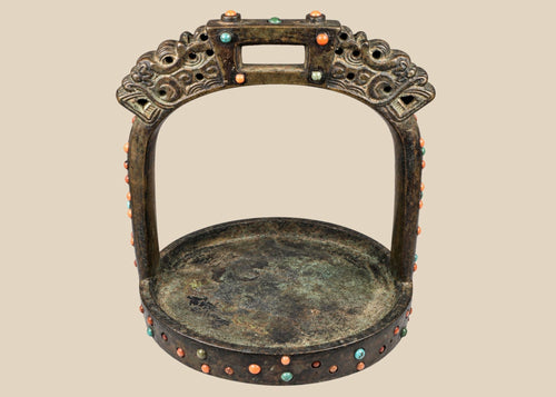 Ornate cast bronze stirrup from Mongolia or Himalayan region, featuring dragon-head terminals, pierced latticework, and hand-set coral, turquoise, and glass inlays, 7 inches tall by 6 inches wide, with natural patina and verdigris, circa 18th century.