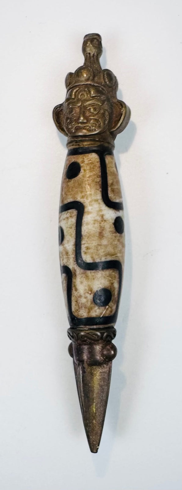Close-up of Tibetan Dzi-style bead with black geometric motifs and metal ritual fittings