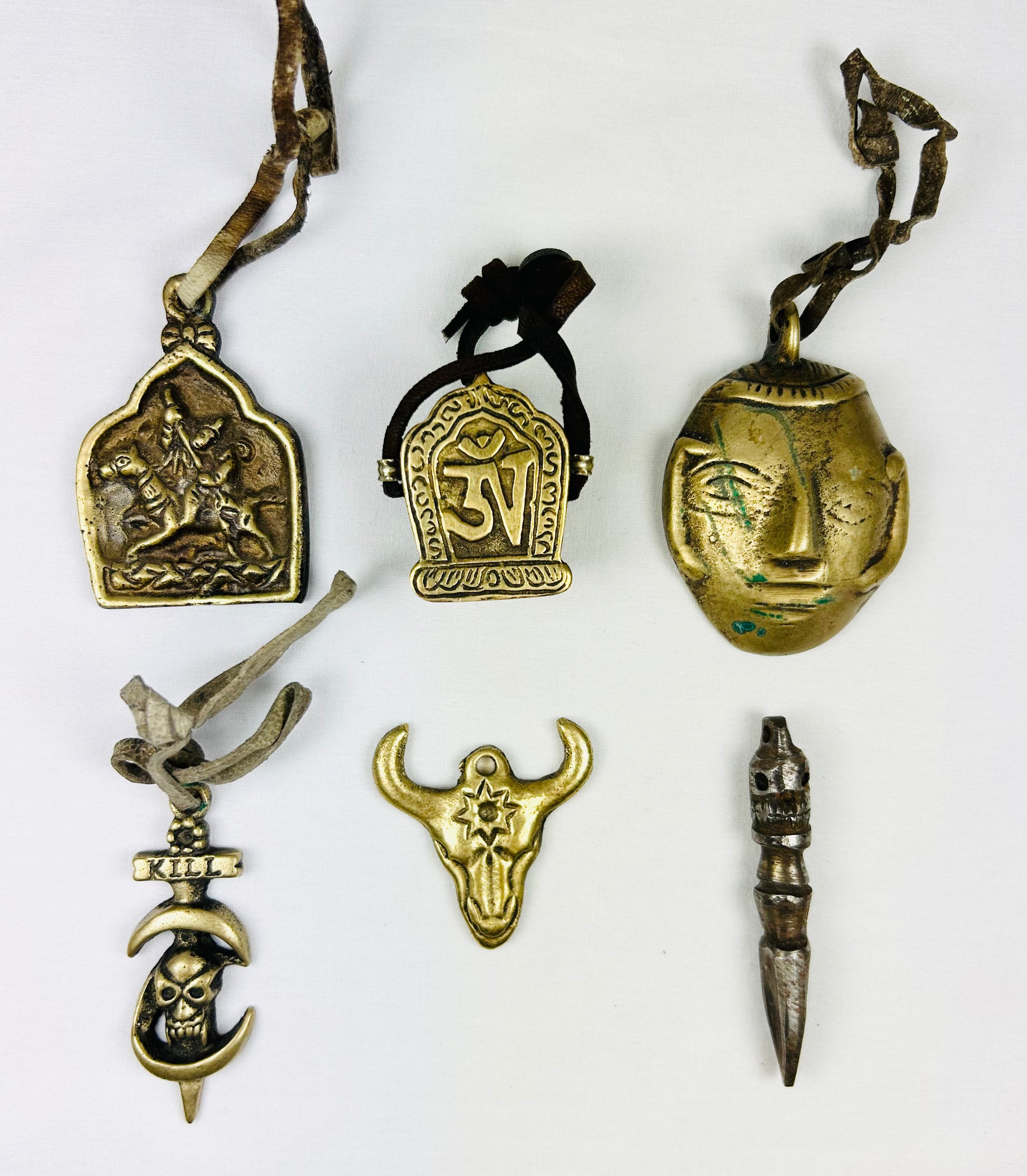 Collection of six Tibetan bronze amulets including St. George, Om Mani Padme Hum, mask, bull head, phurba dagger, and skull “KILL,” all with original leather cords