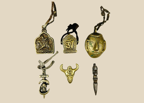 Collection of six Tibetan bronze amulets including St. George, Om Mani Padme Hum, mask, bull head, phurba dagger, and skull “KILL,” all with original leather cords