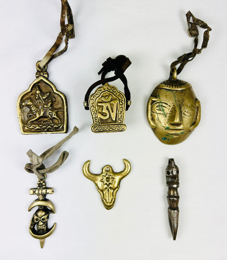 Collection of six Tibetan bronze amulets including St. George, Om Mani Padme Hum, mask, bull head, phurba dagger, and skull “KILL,” all with original leather cords