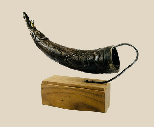 Tibetan bronze ritual powder horn with engraved decorative motifs, curved shape, mounted on a wooden display stand, 19th century.