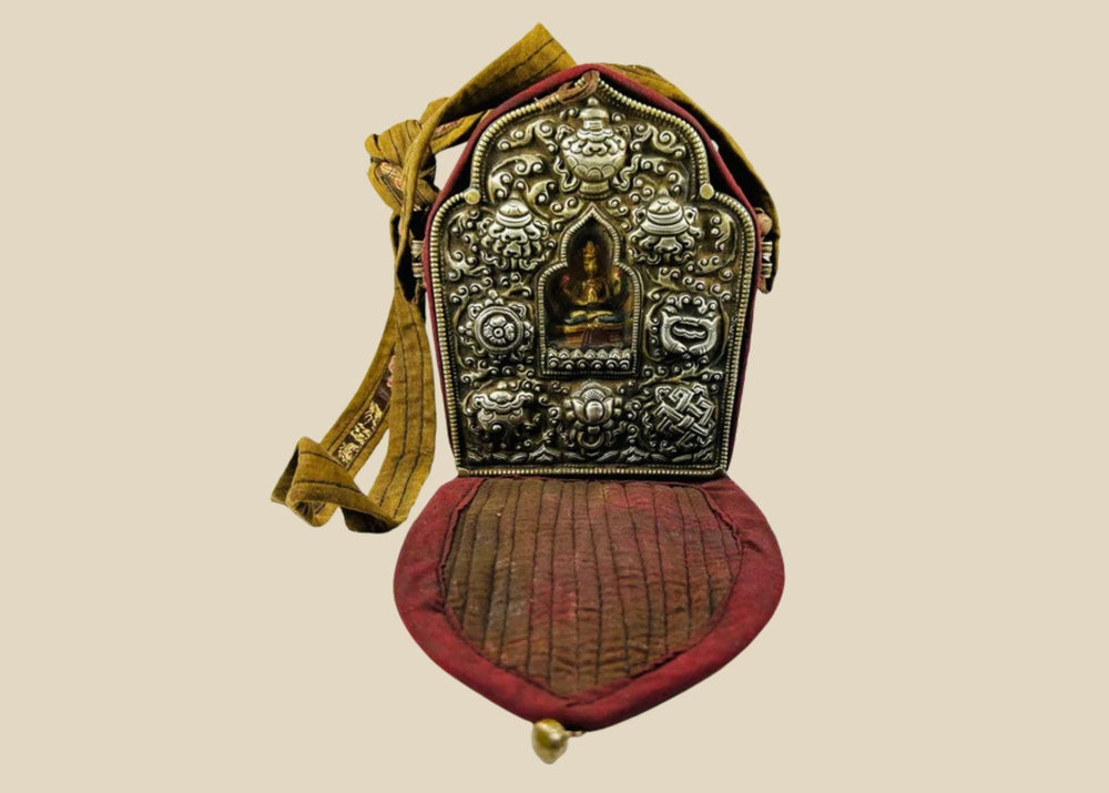 19th-century Tibetan portable shrine (gau) with silver repoussé Buddhist motifs and central glazed Buddha figure, set in embroidered red and gold fabric case with strap, photographed on a white background.