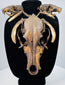 Skull and tooth necklace with layered cord bindings, dark bone cavities, and mottled golden-brown surfaces on a black bust.