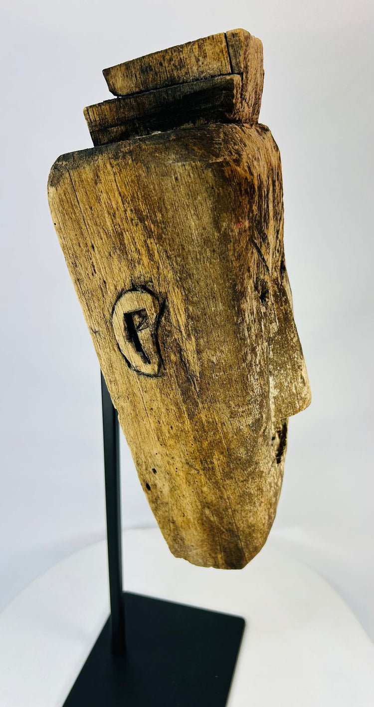 Angled side view of carved tribal mask highlighting expressive grimace, worn patina, and traces of soot from ritual use.