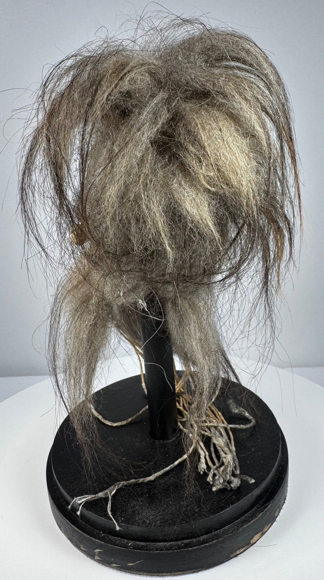 Handcrafted shrunken head-style display object in stitched animal hide with horse hair and museum-style glass presentation.