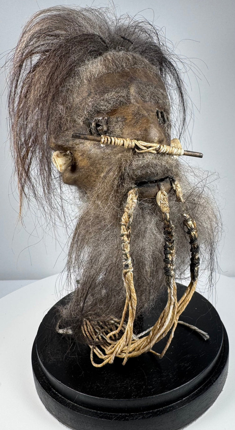 Jivaroan-inspired shrunken head replica displayed beneath a protective glass globe with stitched hide construction and horse hair.