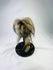 Museum-style replica of a Jivaroan shrunken head, featuring detailed facial stitching, horse hair, and glass globe presentation