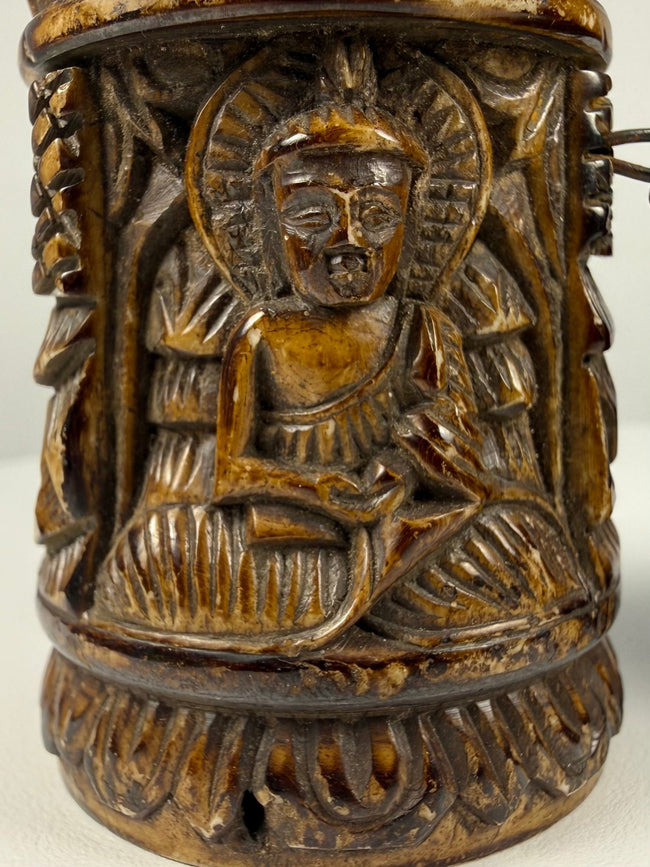Close view of hand-carved Tibetan prayer wheel showing Buddha figures in raised relief