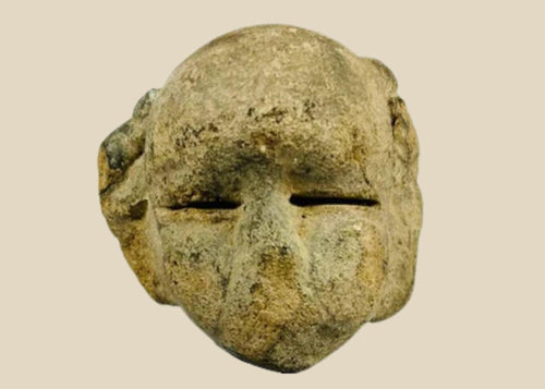 Ancient Mesoamerican stone mask fragment with minimalist facial features and narrow eye slits, carved from a single block of stone and mounted on a black wooden display stand, dating to 500 BCE–500 CE.