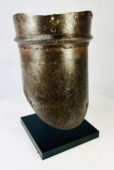16th-century European upper arm armor, cannon-style plate with scalloped edge detailing, aged patina, and mounted on a display stand.