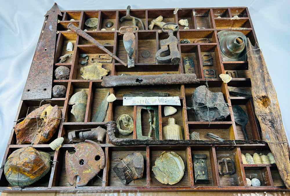 American Civil War shadow-box display of dug relics from the Battle of Vicksburg, Mississippi Valley, circa 1861–1865, featuring Minie balls, carved bullets, artillery and shell fragments, US plate and eagle breastplate pieces, spurs, stirrups, buckles, canteen spout, pipe bowl, glass bottle, camp hardware, all mounted in a wooden tray with wire supports and historic hand-written label