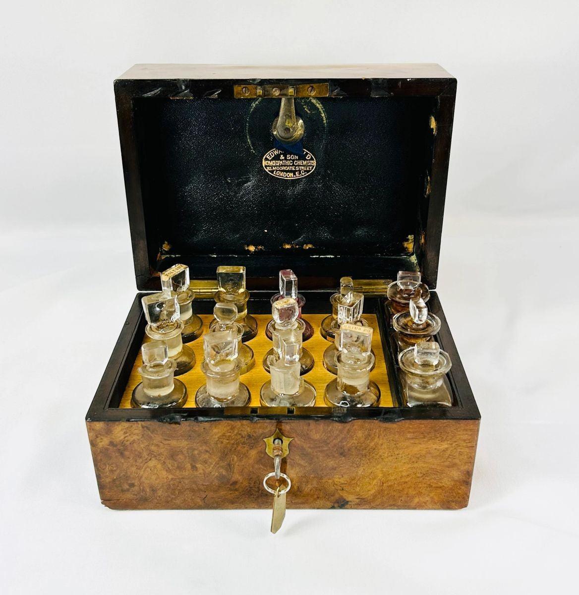 Victorian apothecary box by Edward Gould & Son, London, late 19th century. Burl wood case with brass fittings, velvet-lined interior, and twelve original labeled glass bottles with stoppers, including Arnica Montana, Belladonna, and Bryonia Alba. Reflects Victorian homeopathy, craftsmanship, and medical history.