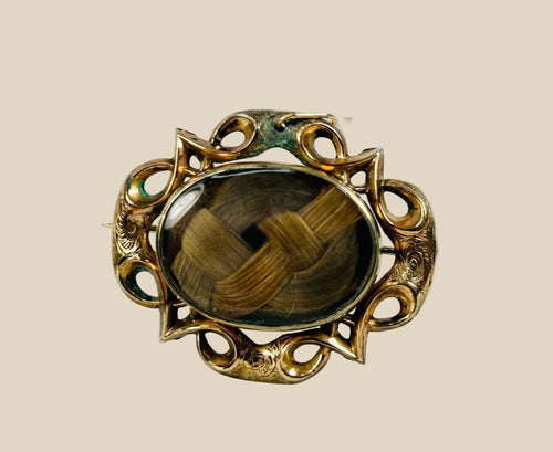 Antique Victorian mourning brooch with braided human hair under beveled glass, set in an ornate gold-plated brass Gothic Revival frame, circa 1850–1880.