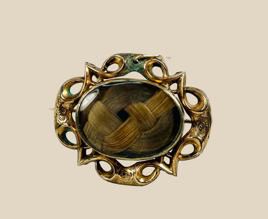 Antique Victorian mourning brooch with braided human hair under beveled glass, set in an ornate gold-plated brass Gothic Revival frame, circa 1850–1880.