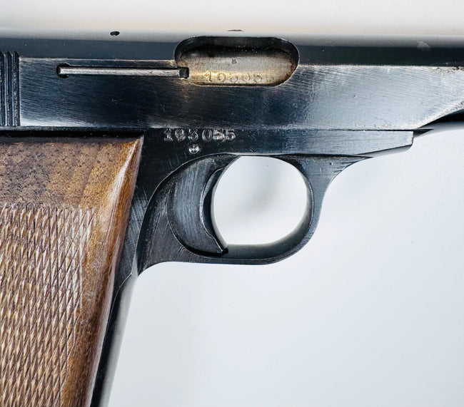 Close-up of the FN Browning Model 1922’s ejection port, curved trigger, and worn steel beside the walnut grip.