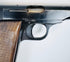 Close-up of the FN Browning Model 1922’s ejection port, curved trigger, and worn steel beside the walnut grip.