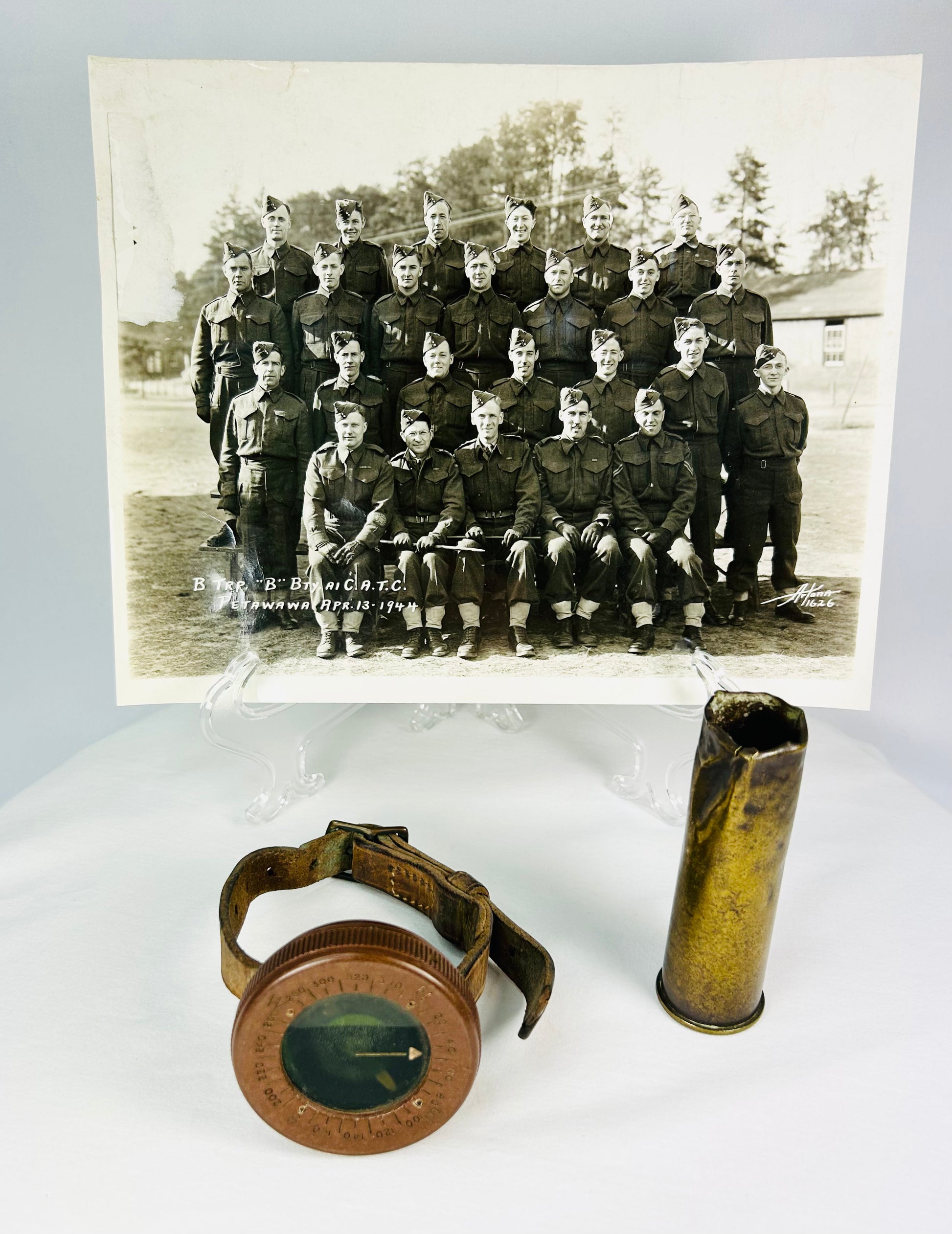 Vintage WWI military memorabilia set including a soldier’s wrist compass, a spent shell casing, and a sepia-toned unit photograph of troops, displayed on a white background.