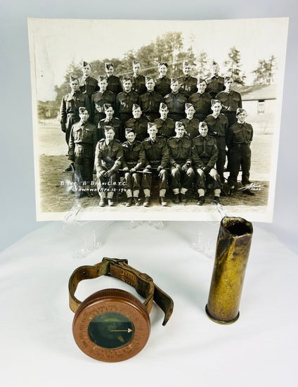 Vintage WWI military memorabilia set including a soldier’s wrist compass, a spent shell casing, and a sepia-toned unit photograph of troops, displayed on a white background.