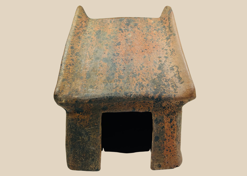 Pre-Columbian West Mexico terracotta architectural house model with peaked roof and doorway on beige background.