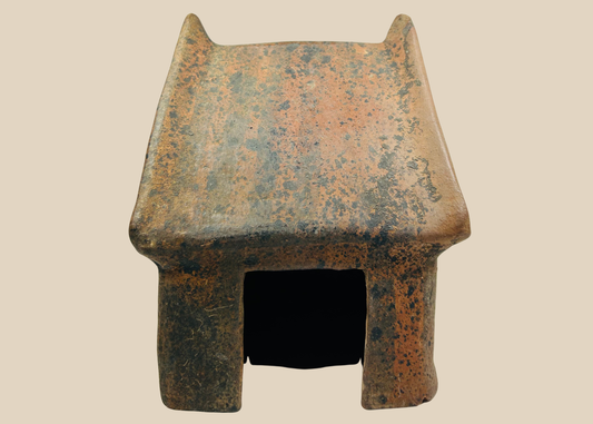 Pre-Columbian West Mexico terracotta architectural house model with peaked roof and doorway on beige background.