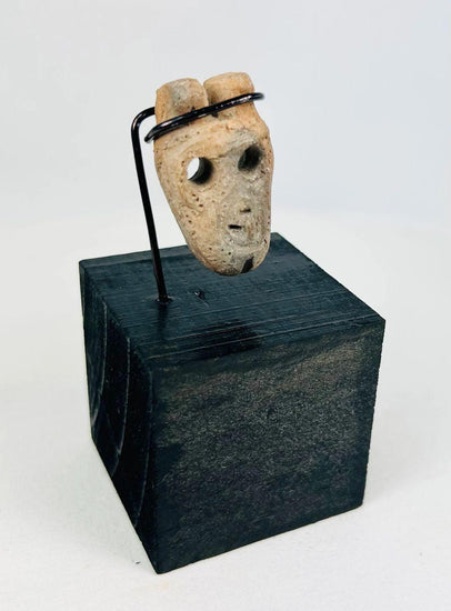 Miniature anthropomorphic mask pendant carved from bone, featuring hollowed eyes, prominent nose ridge, open mouth, and twin suspension holes; mounted on custom display stand; Western Mexico, Colima/Nayarit region, circa 300 BCE–300 CE.